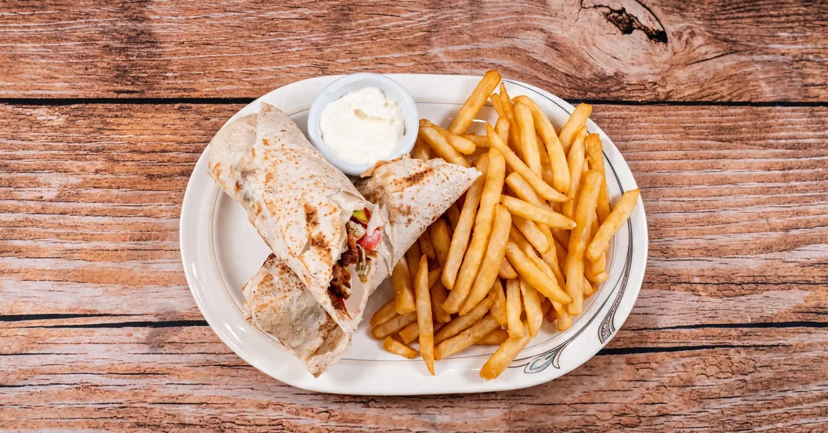 A chicken shawarma wrap cut in half, with golden fries and garlic sauce