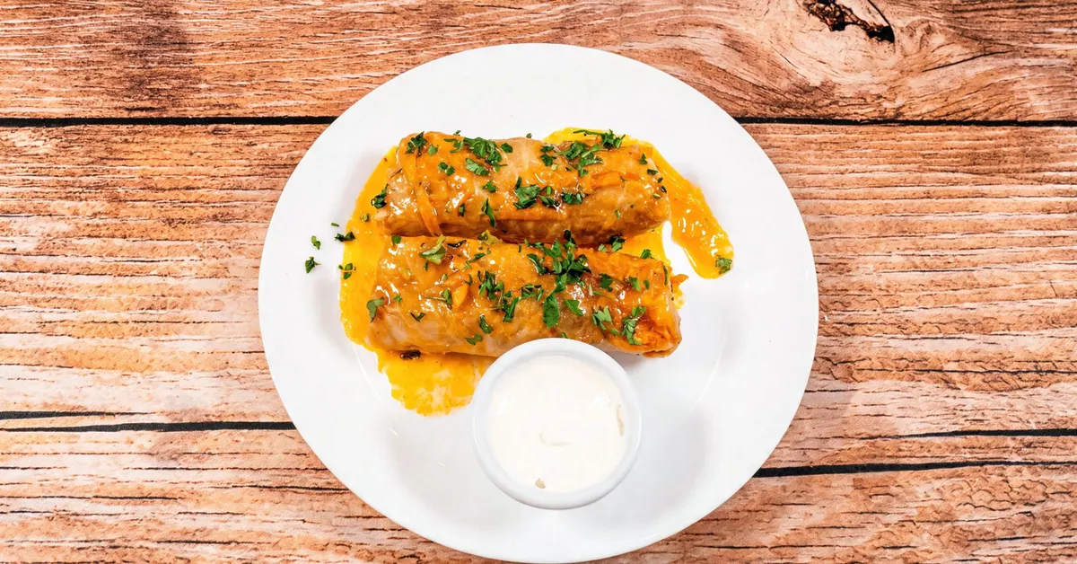 Two Ukrainian holubtsi cabbage rolls in a carrot-tomato sauce, with sour cream