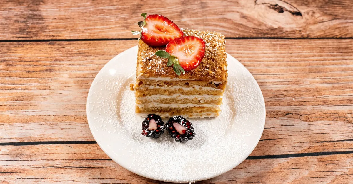 A layered slice of honey cake with fresh strawberries and blackberries