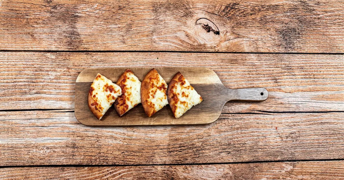 Cheese manaeesh fresh from the oven, cut into quarters on a wooden board