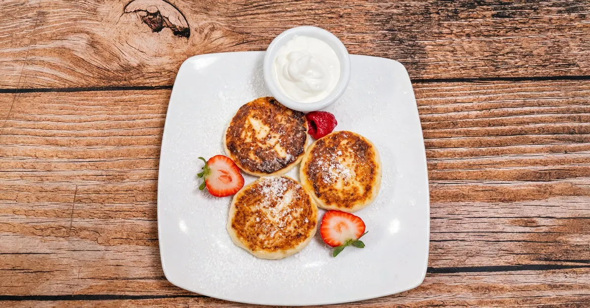 Three golden syrnyky cheese pancakes with sour cream and fresh berries